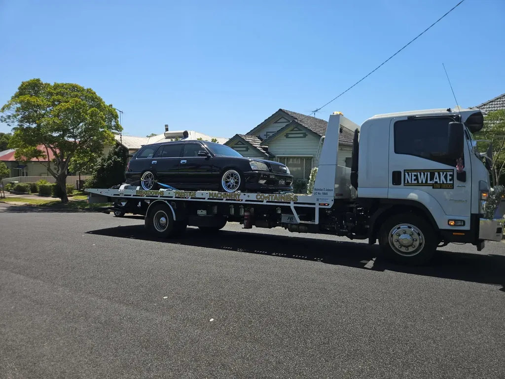 NewLake tow truck with a black Toyota Crown wagon loaded on the tray on a Newcastle street.