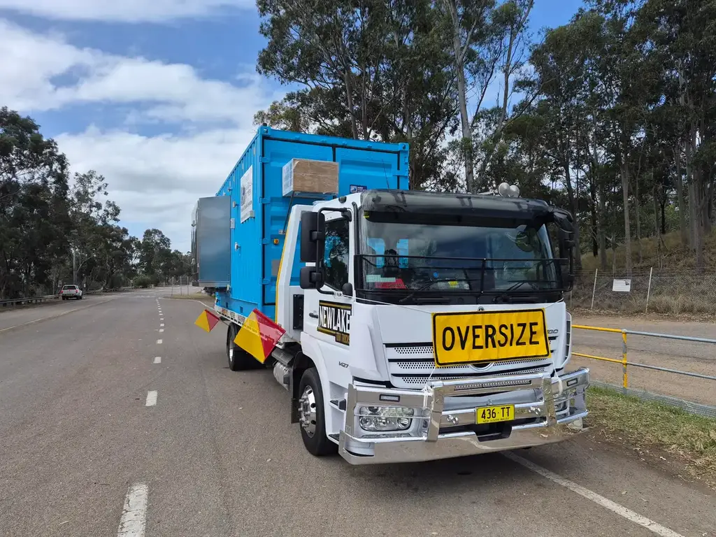 NewLake tow truck transporting a blue water treatment container on a rural road